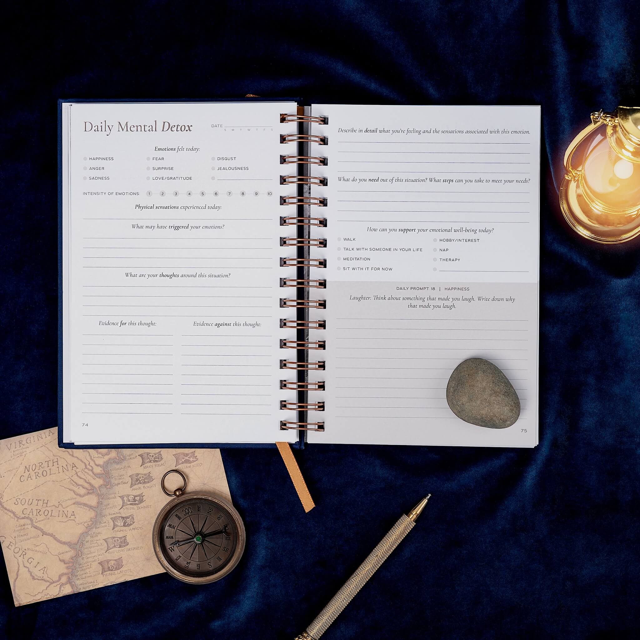 Open notebook on a dark fabric background with a compass, stone, and decorative light.